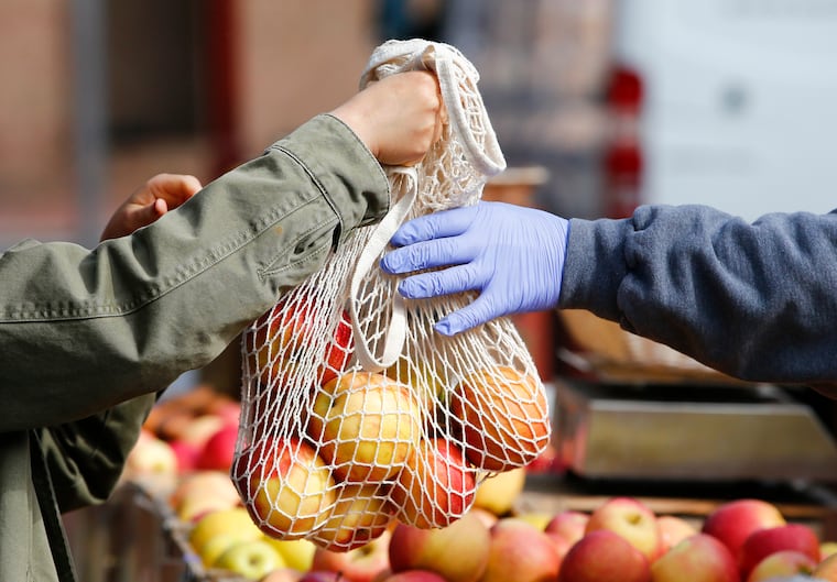 A shopper receives apples from a gloved vender from the Beechwood Orchards at the Headhouse Farmers Market in the Society Hill section of Philadelphia on Sunday, March 22, 2020.